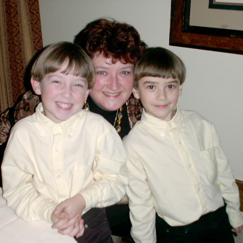 Old family photo of a smiling woman sitting behind two young boys in matching pale yellow button-down shirts